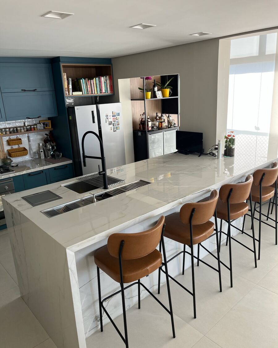 Ilha de cozinha em pedra clara com cuba e banquetas, integrada à sala